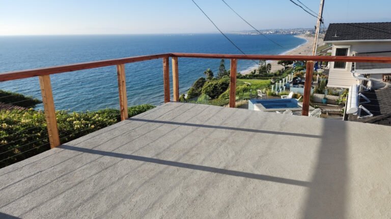 Ocean view from a balcony with wooden railing overlooking coastal homes.