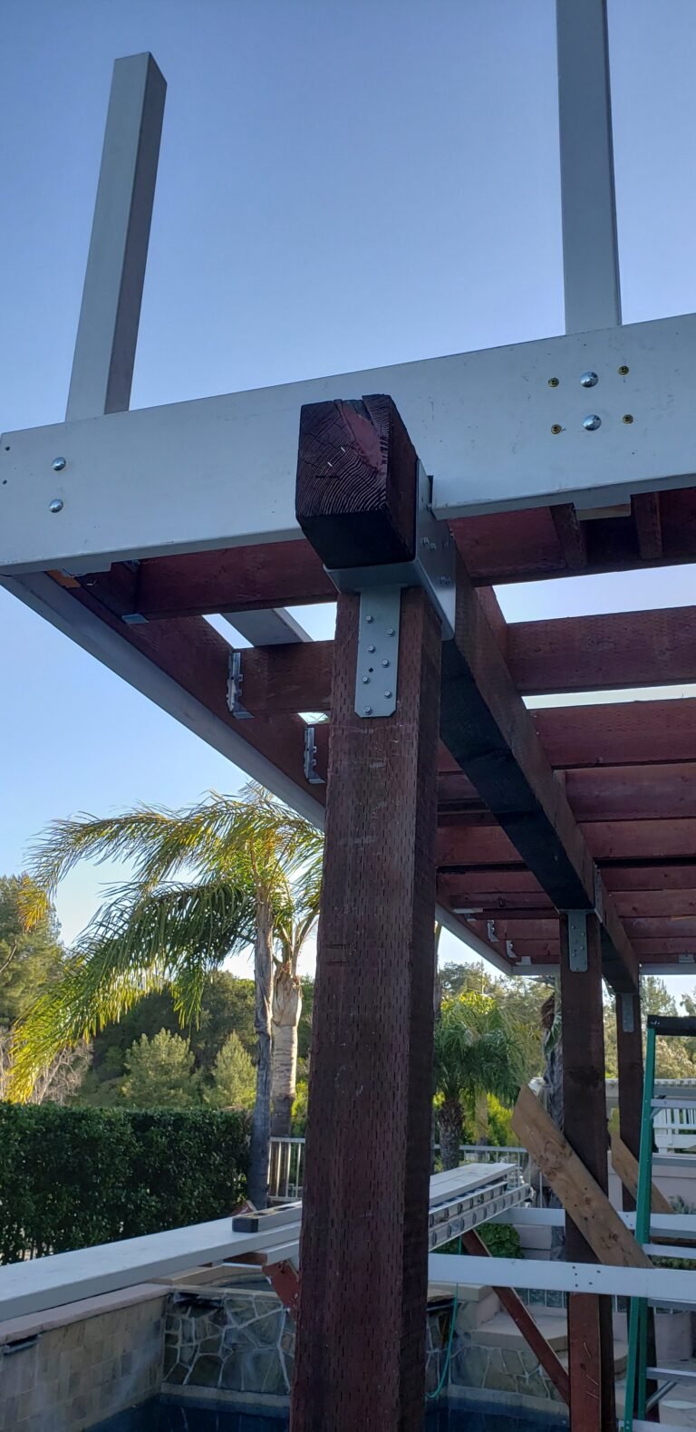Framing of a raised outdoor deck with redwood posts and beams secured by metal brackets.