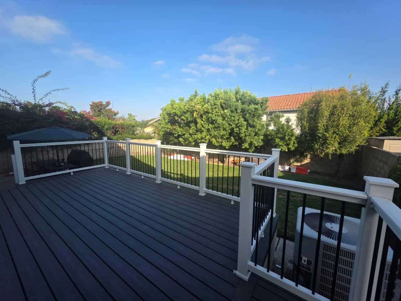Composite deck with black balusters combined white top rail and bottom rails with vibrant bushes and trees in the background